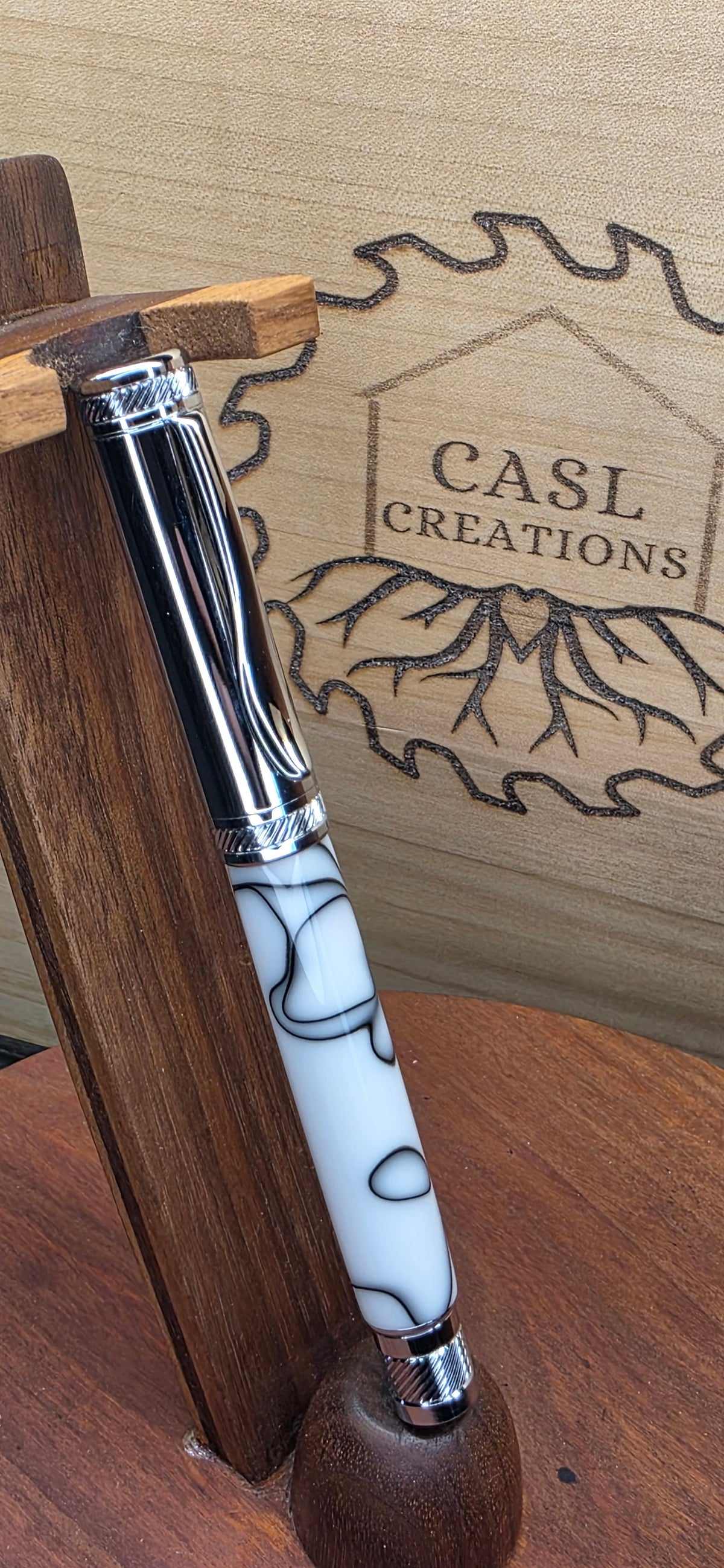 White-and-black patterned pen with chrome hardware on a wooden stand beside the CASL Creations logo.